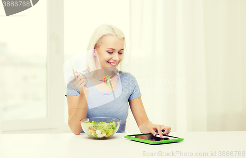 Image of smiling woman eating salad with tablet pc at home