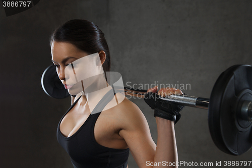 Image of young woman flexing muscles with barbell in gym