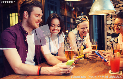 Image of happy friends with smartphones and drinks at bar