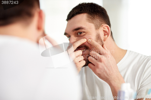 Image of smiling man squeezing pimple at bathroom mirror
