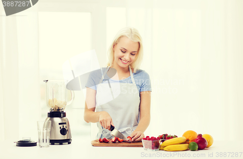 Image of smiling woman with blender preparing shake at home