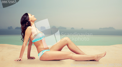 Image of happy woman tanning in bikini over swimming pool