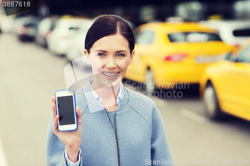 Image of smiling woman showing smartphone over taxi in city