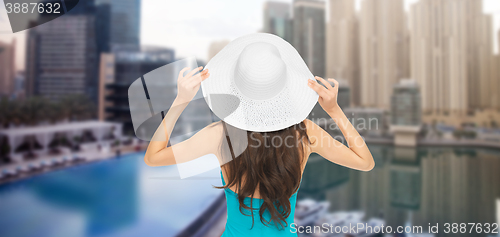 Image of woman in swimsuit and sun hat from back over city