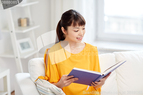 Image of smiling young asian woman reading book at home