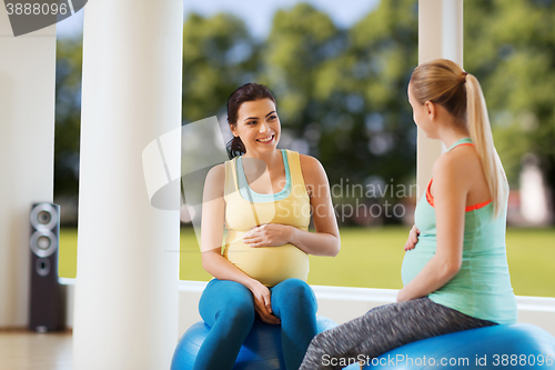 Image of two happy pregnant women sitting on balls in gym