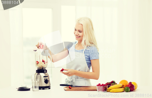 Image of smiling woman with blender preparing shake at home