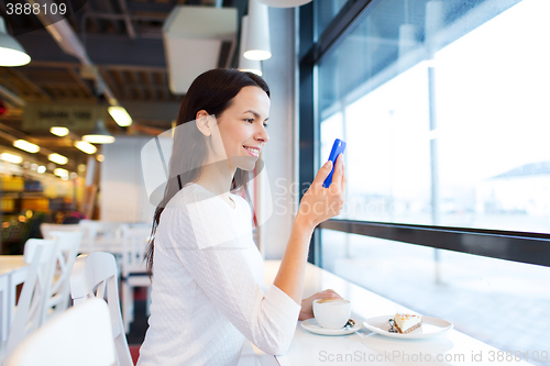 Image of smiling woman with smartphone and coffee at cafe