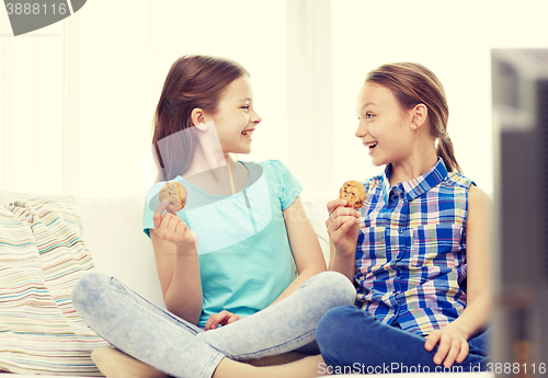 Image of happy girls watching tv and eating cookies at home