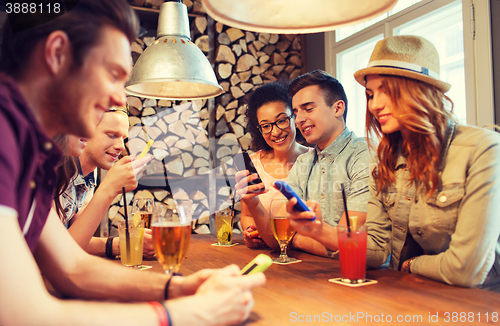 Image of happy friends with smartphones and drinks at bar