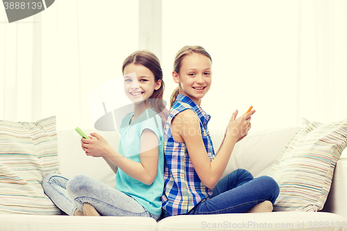 Image of happy girls with smartphones sitting on sofa