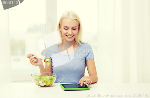 Image of smiling woman eating salad with tablet pc at home