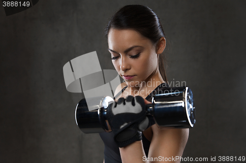 Image of young woman flexing muscles with dumbbells in gym