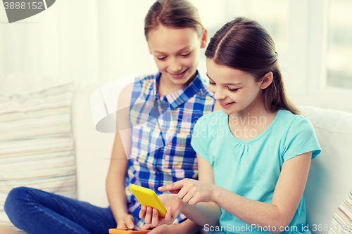 Image of happy girls with smartphones sitting on sofa