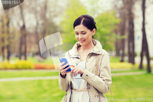 Image of smiling woman calling on smartphone in park