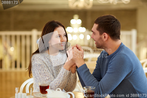 Image of happy couple with tea holding hands at restaurant