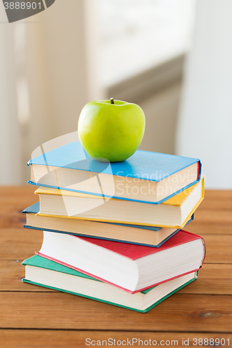 Image of close up of books and green apple on wooden table