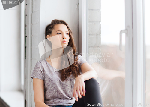 Image of sad pretty teenage girl sitting on windowsill