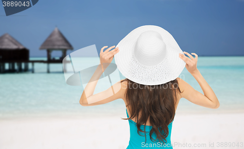 Image of woman in swimsuit and sun hat from back on beach
