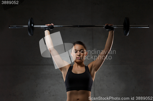 Image of young woman flexing muscles with barbell in gym