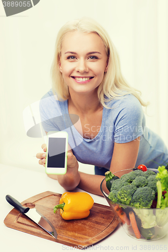 Image of smiling woman with smartphone cooking vegetables