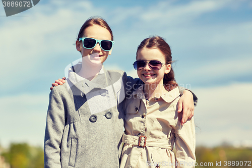 Image of happy little girls in sunglasses hugging outdoors