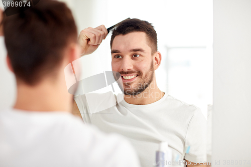 Image of happy man brushing hair  with comb at bathroom