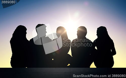 Image of silhouettes of friends sitting on stairs over sun