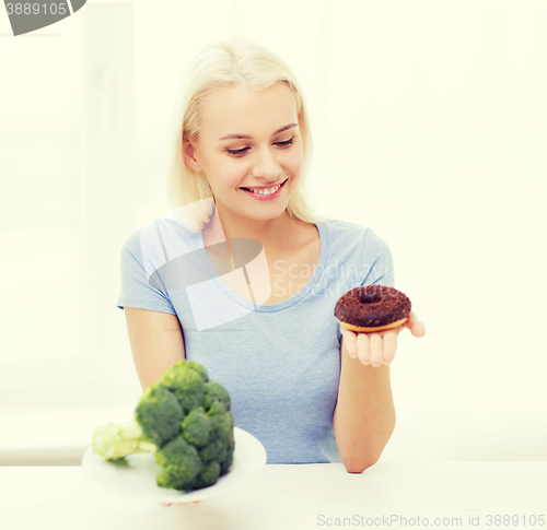 Image of smiling woman with broccoli and donut at home