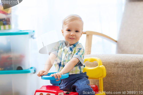 Image of happy little baby boy driving ride-on car at home