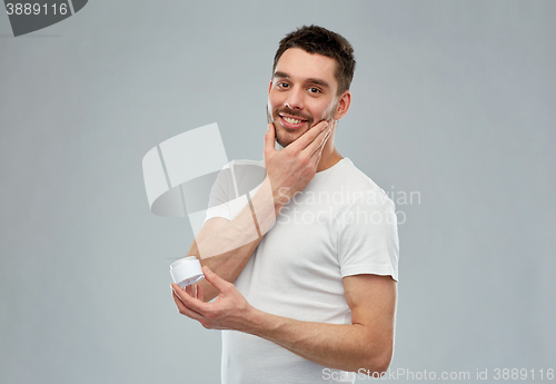 Image of happy young man applying cream to face over gray