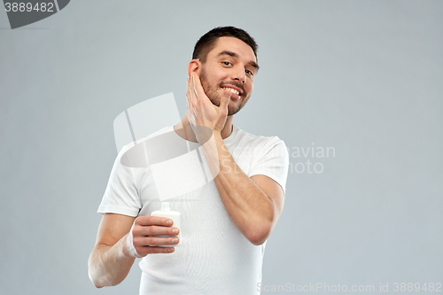 Image of happy young man applying cream or lotion to face