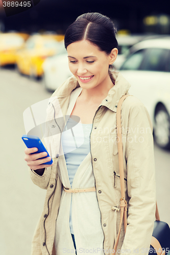 Image of smiling woman with smartphone over taxi in city