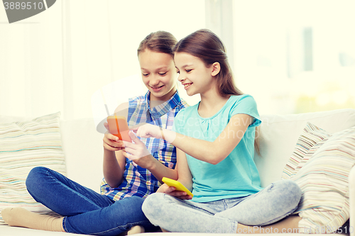 Image of happy girls with smartphones sitting on sofa