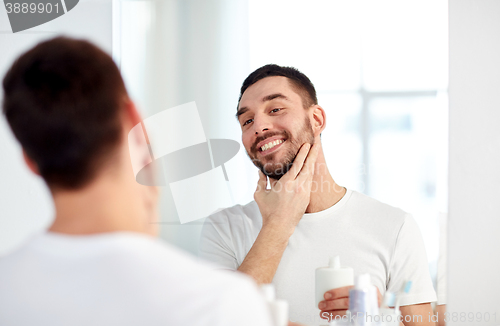 Image of happy man applying aftershave at bathroom mirror