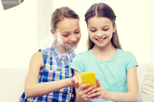 Image of happy girls with smartphone sitting on sofa