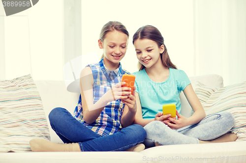Image of happy girls with smartphones sitting on sofa