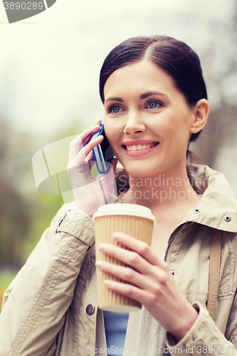 Image of smiling woman with smartphone and coffee in park