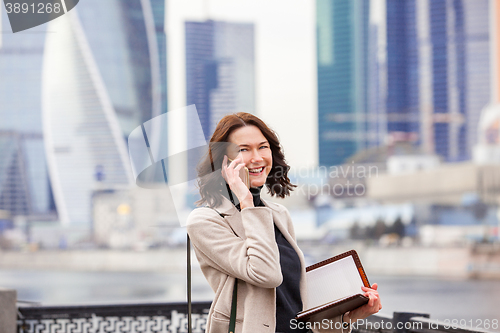 Image of smiling middle-aged woman with notebook talking on the phone