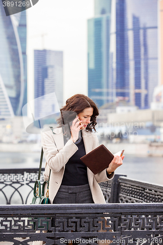 Image of woman in a bright coat with notebook talking on mobile