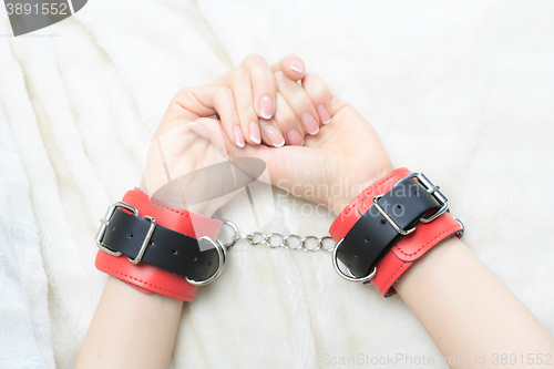 Image of female hands in leather handcuffs. on the background sheet. sex toys.