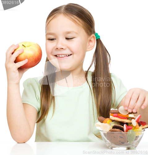 Image of Little girl choosing between apples and sweets