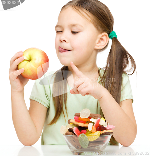 Image of Little girl choosing between apples and sweets