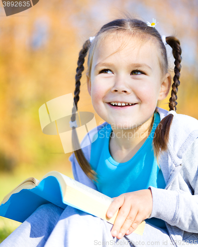 Image of Little girl is reading a book outdoors