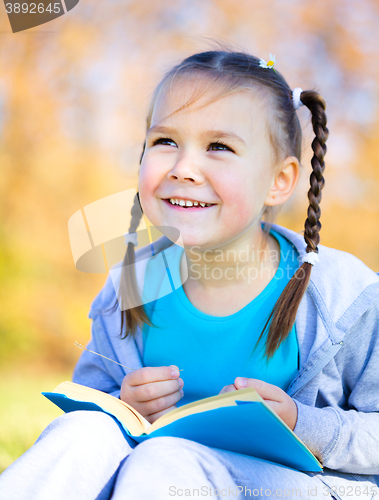 Image of Little girl is reading a book outdoors