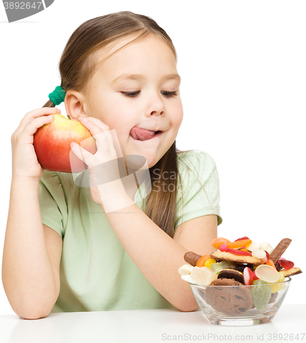 Image of Little girl choosing between apples and sweets