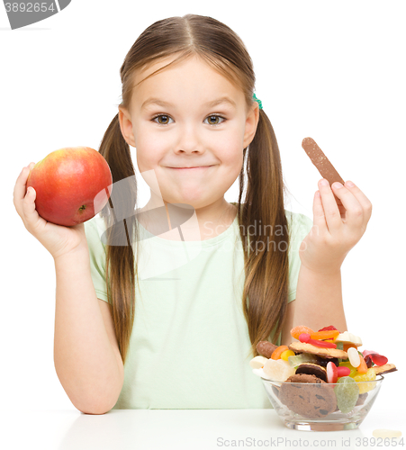 Image of Little girl choosing between apples and sweets