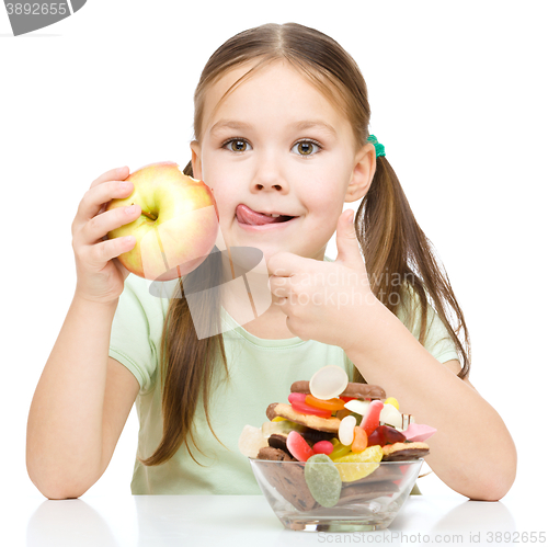 Image of Little girl choosing between apples and sweets