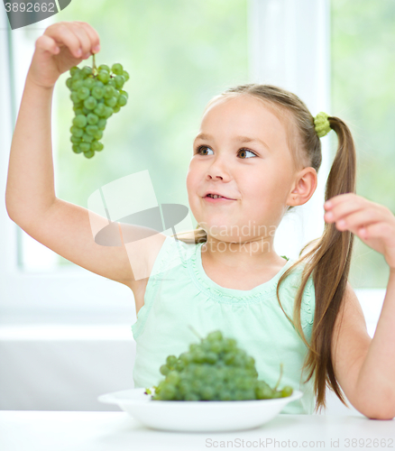 Image of Cute little girl is looking at green grapes