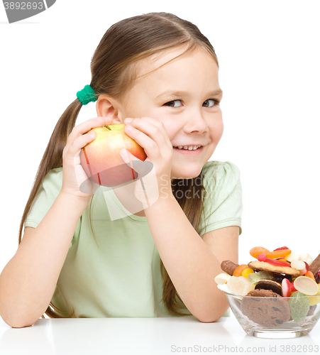 Image of Little girl choosing between apples and sweets